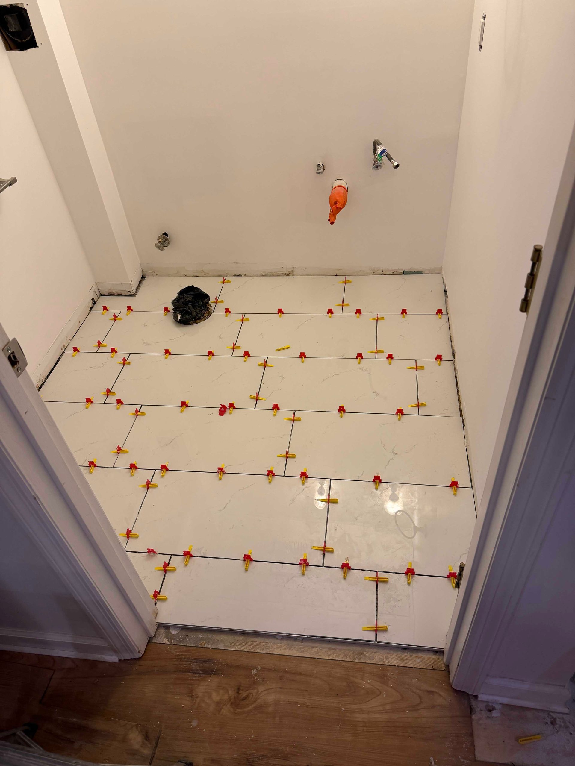 White tiles being laid on a bathroom floor with leveling spacers in place.