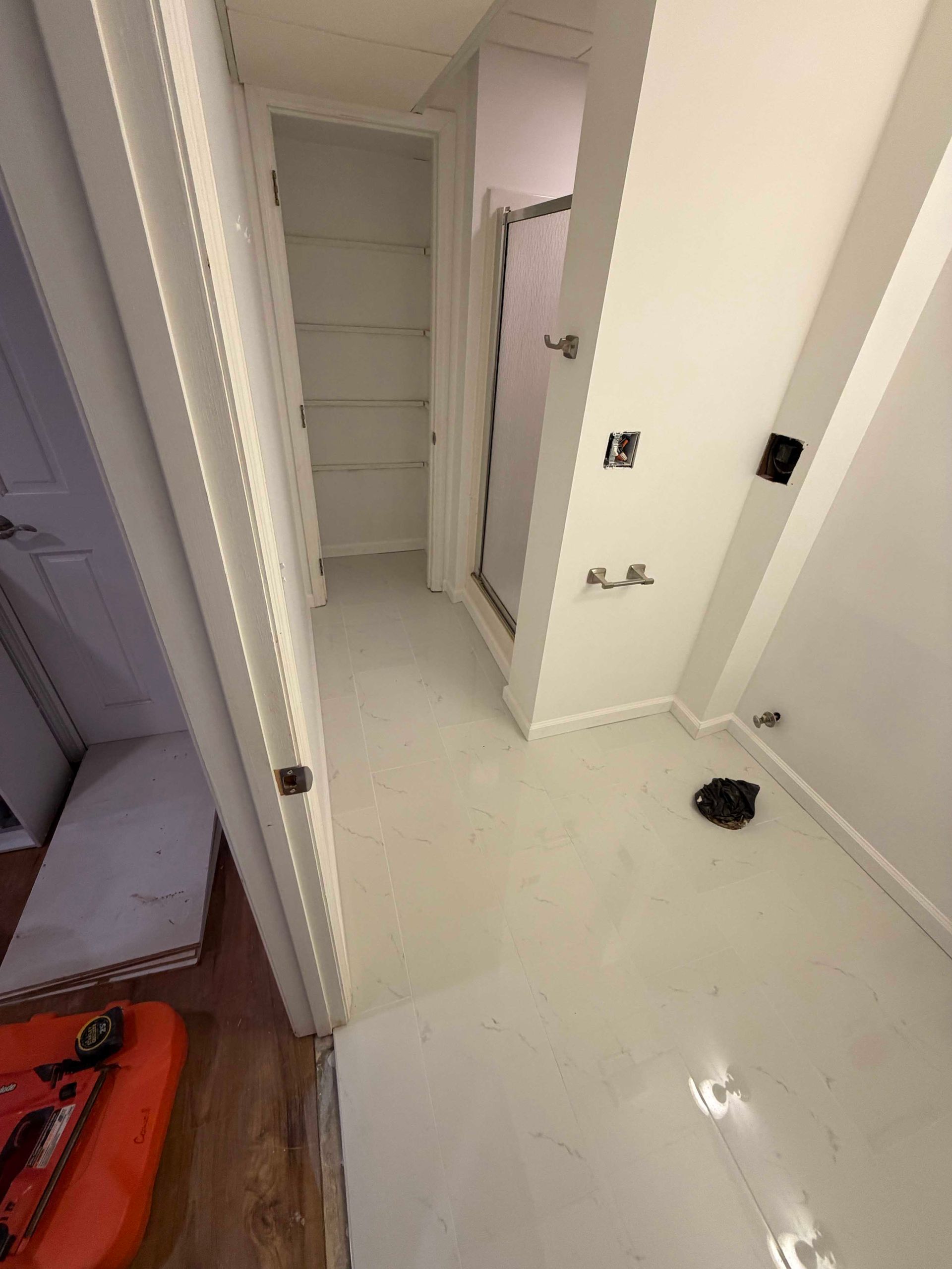 Bathroom with white walls and floor, shower, closet, and open doorway.