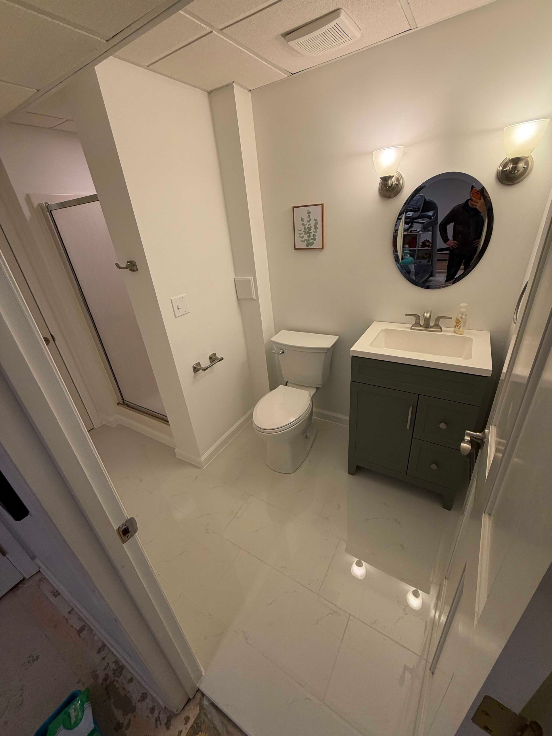 Bathroom with white tile, a green vanity, and a round mirror.