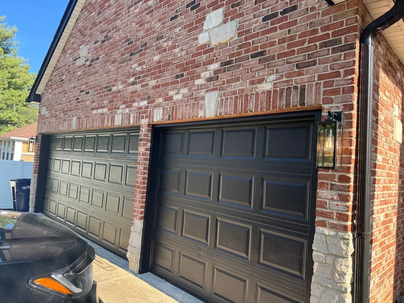Two black garage doors on a brick building with a decorative light fixture.