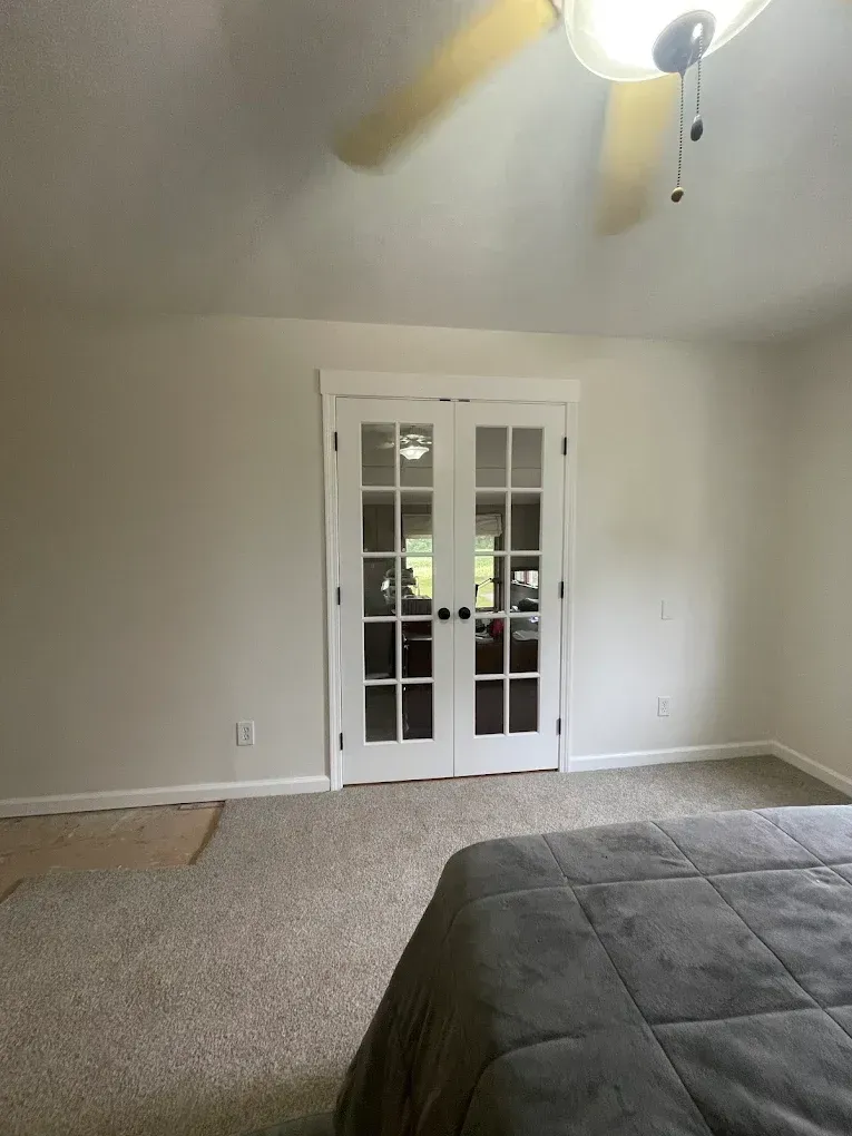 Bedroom with French doors, beige walls, carpet, and a gray comforter on the bed.