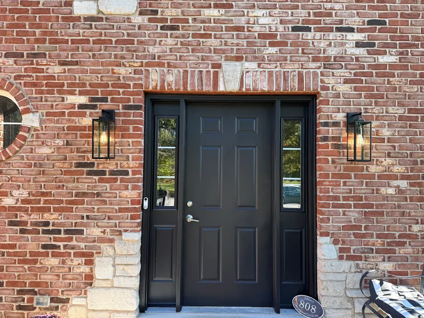 Black front door with sidelights, flanked by brick, sconces, and stone accents.