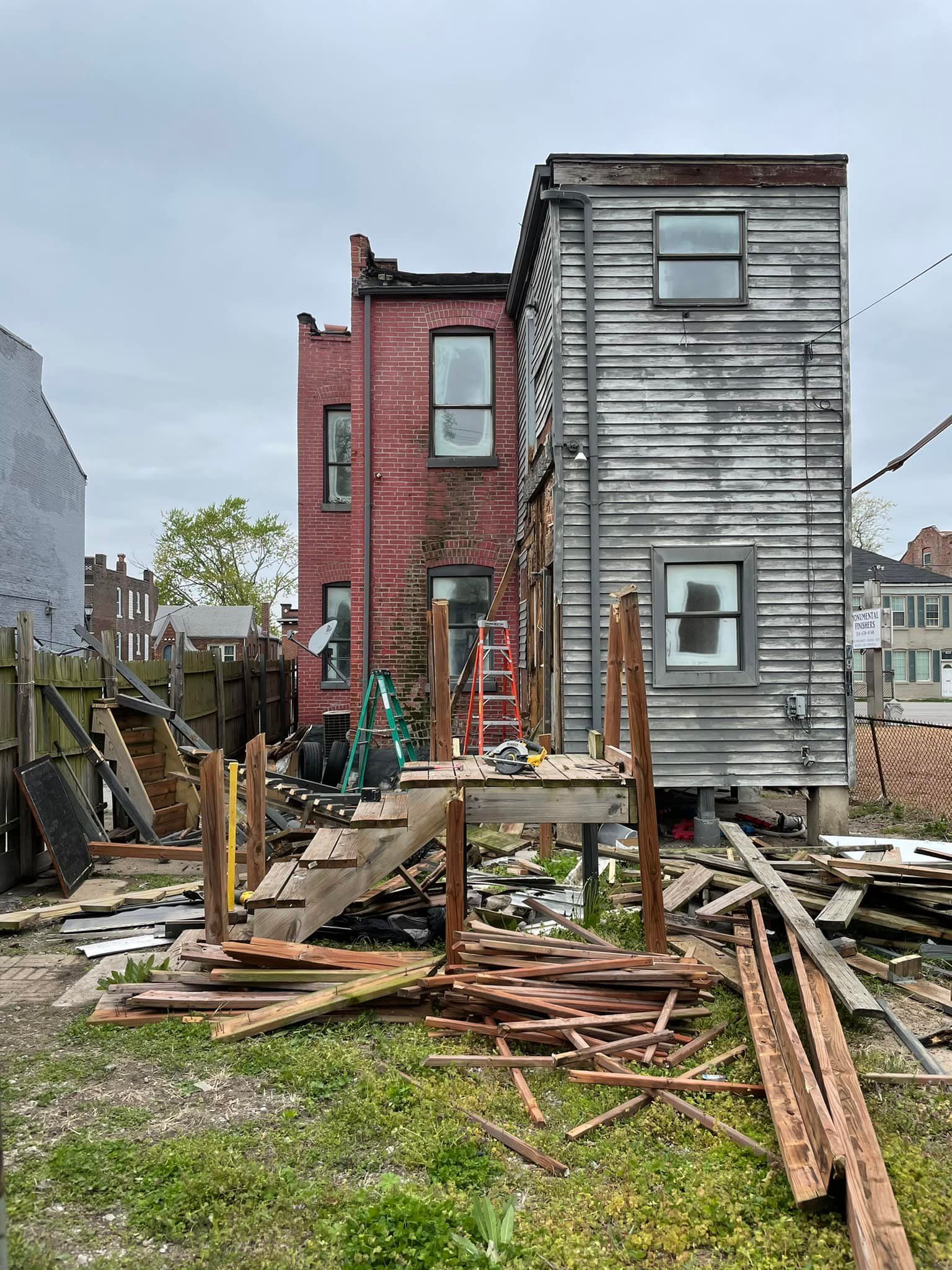 Backyard scene with construction in progress, wooden deck, red brick building, and weathered wood siding.