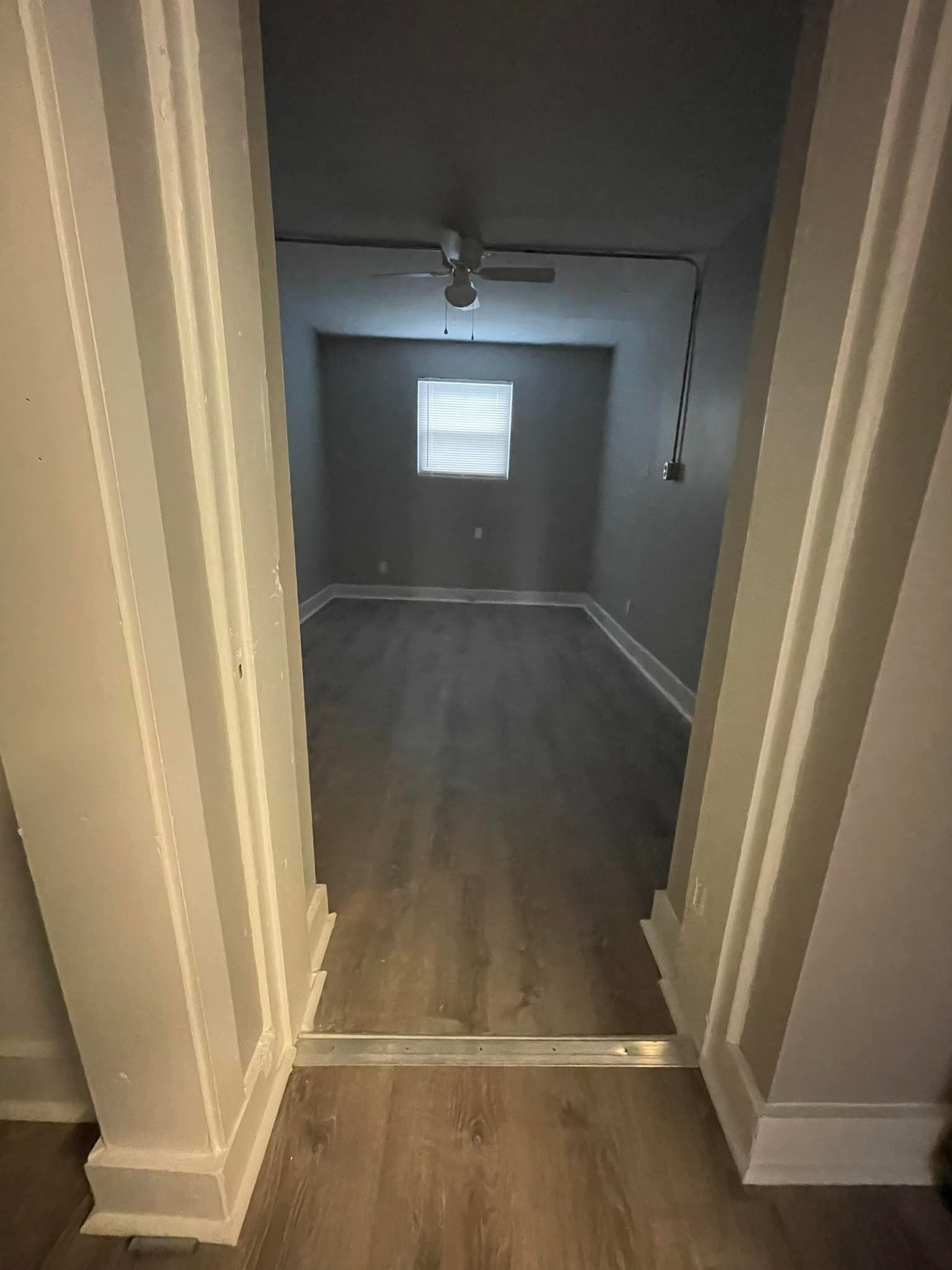 View of a room through a doorway. Gray walls, wood-look flooring, window.