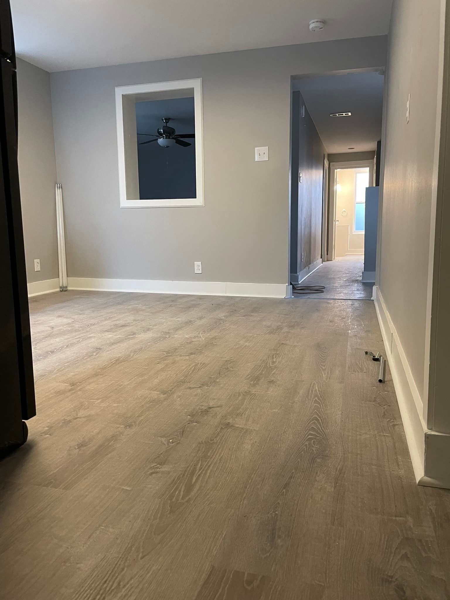 Empty room with gray walls, wood-look flooring, and a hallway entrance.