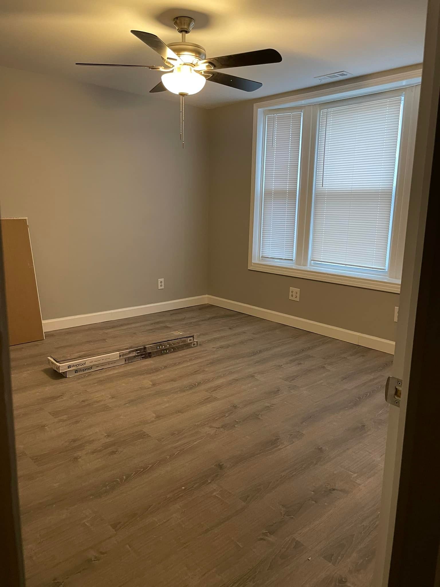 Empty room with gray walls, wood-look flooring, ceiling fan, and window with blinds.