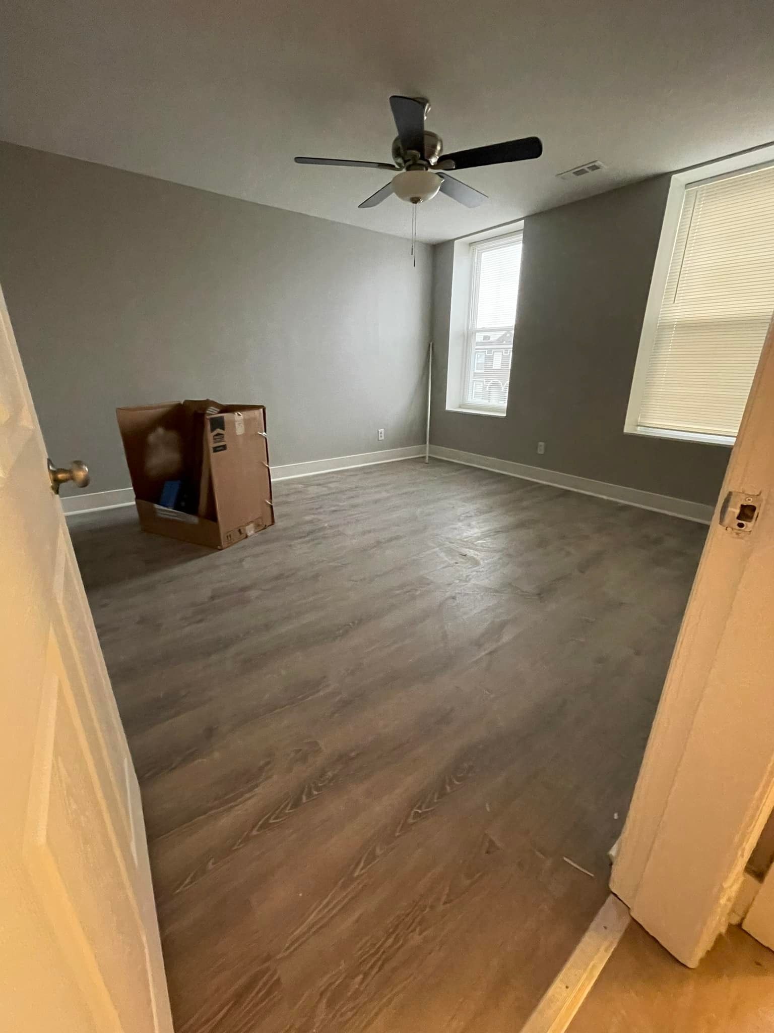 Empty room with gray walls, wood-look flooring, ceiling fan, and window with blinds.