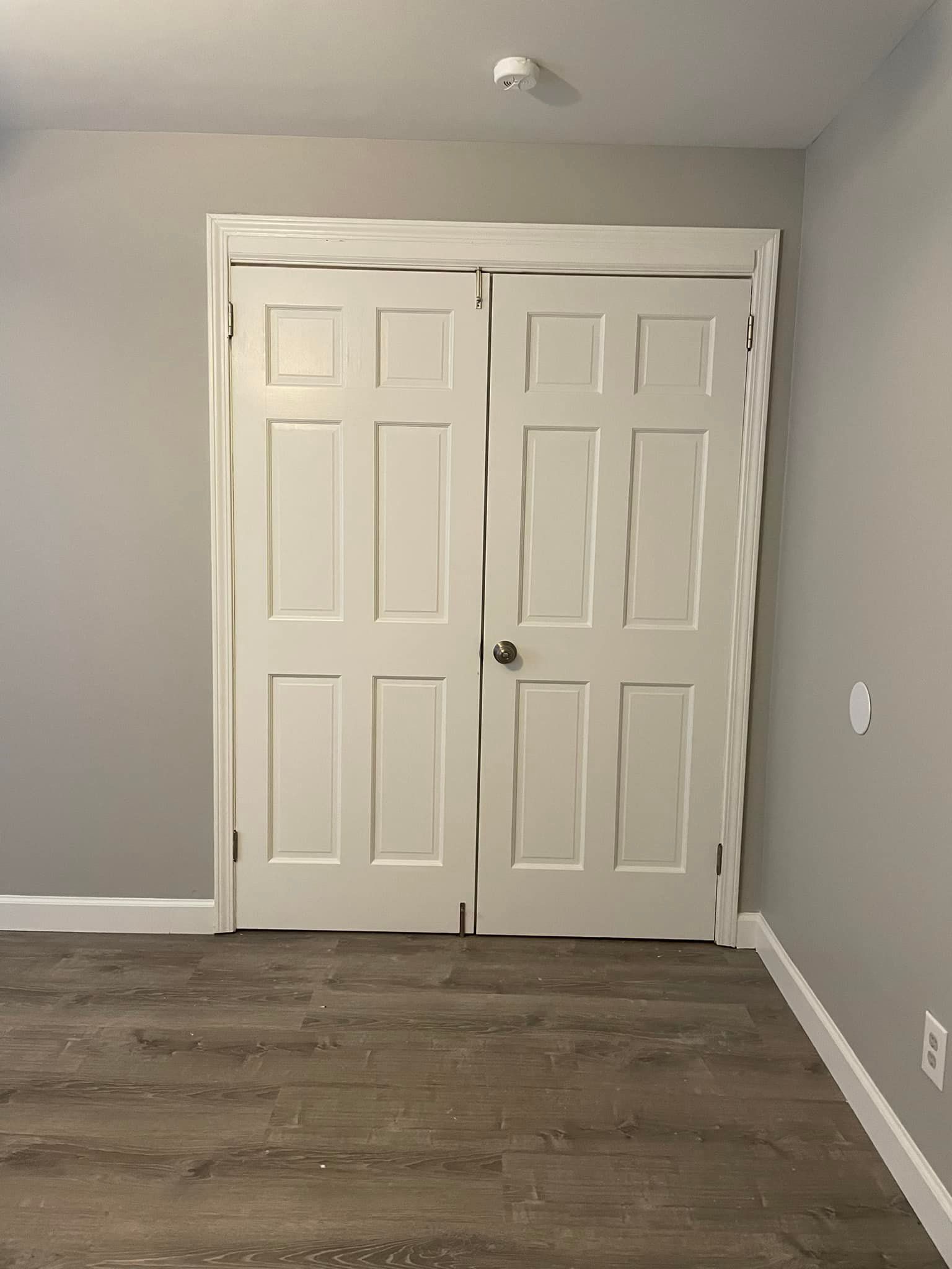 White closet doors in a room with gray walls and wood-look flooring.