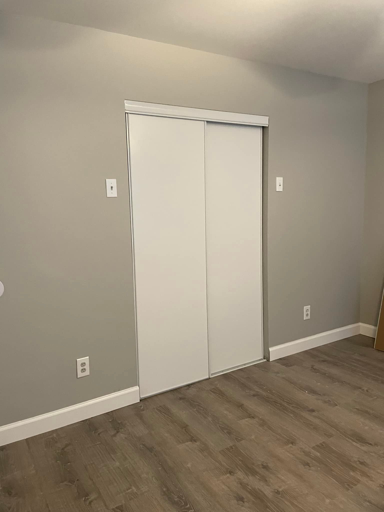 A room with gray walls, white trim, and a light-wood-look floor. Sliding closet doors are closed.