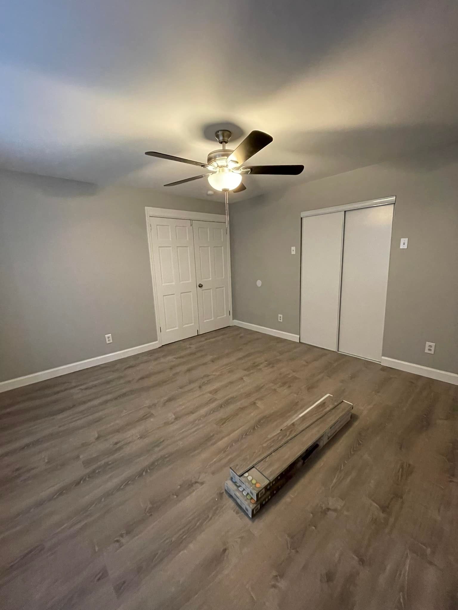 Empty bedroom with gray walls, wood-look flooring, white doors, and a ceiling fan.
