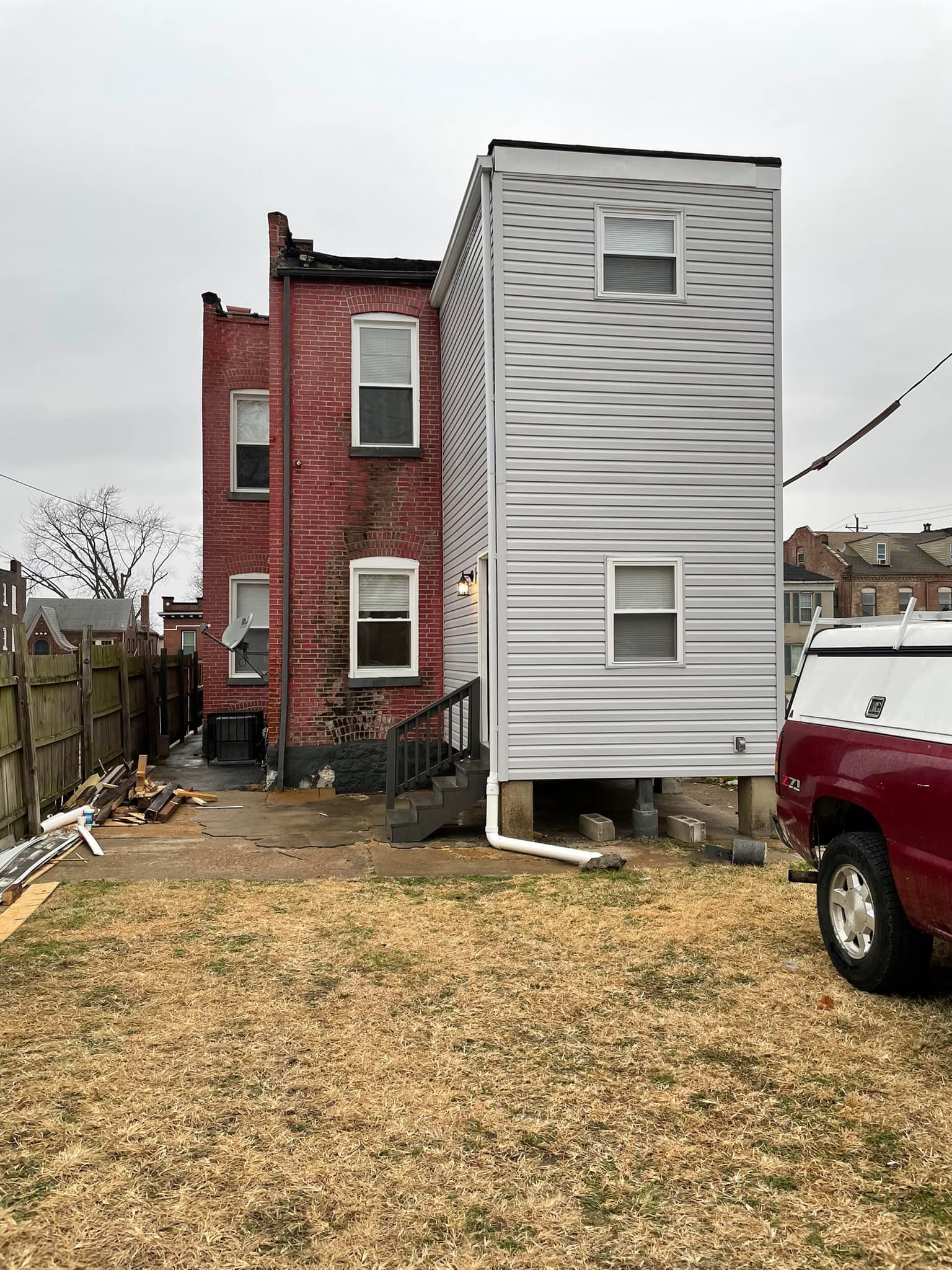 Rear view of a two-story house with red brick and grey siding, partially obscured by a red truck in the yard.