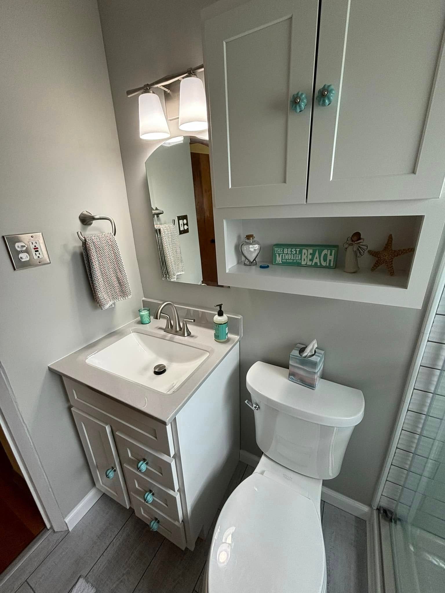 Small bathroom with a white toilet, sink, and cabinet. Gray walls, a mirror, and decorative seashells.