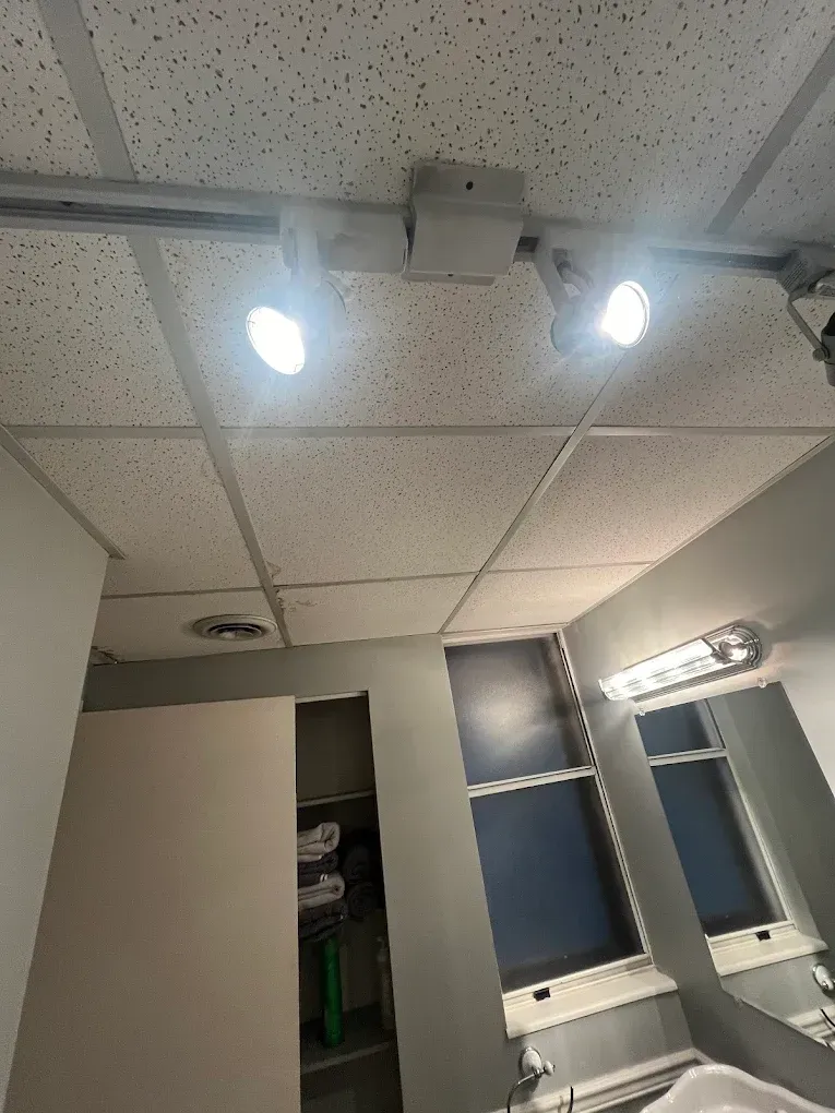 Overhead view of a ceiling with track lighting, above a small room with a window and a partly open closet.