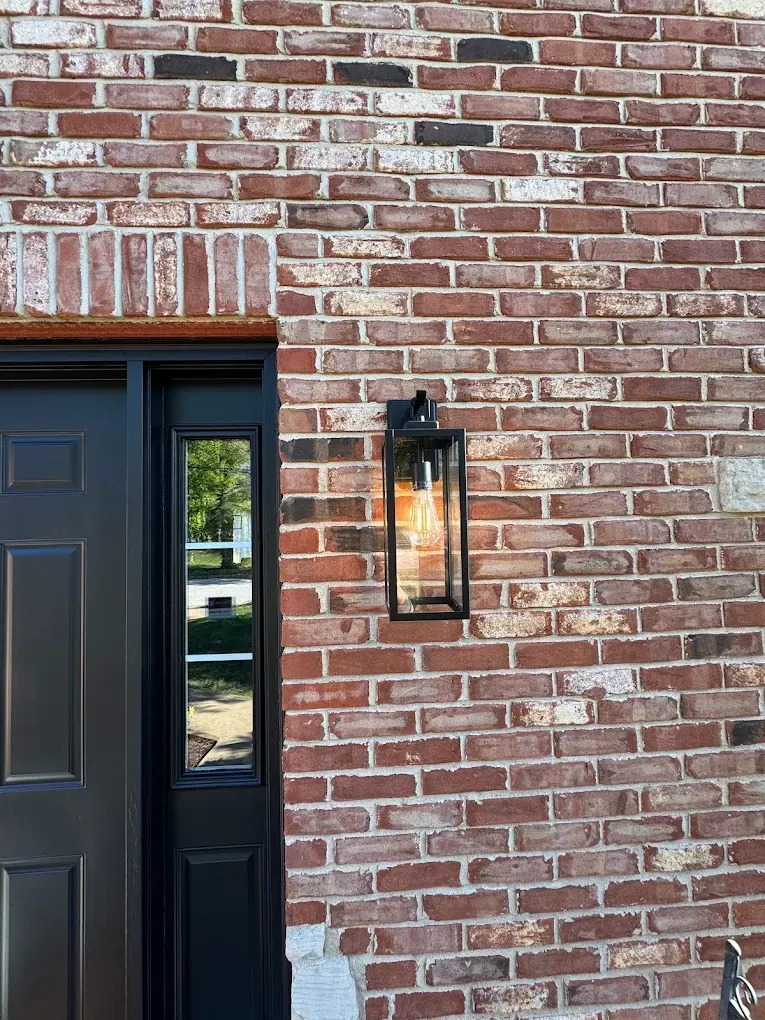 Black door and sidelight next to brick wall with a black lantern-style light fixture.