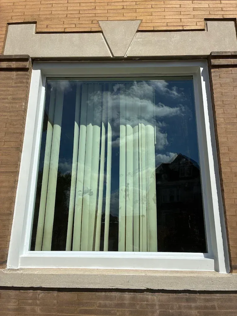 Window with white frame, reflected sky and clouds, beige curtains, set in brick wall.