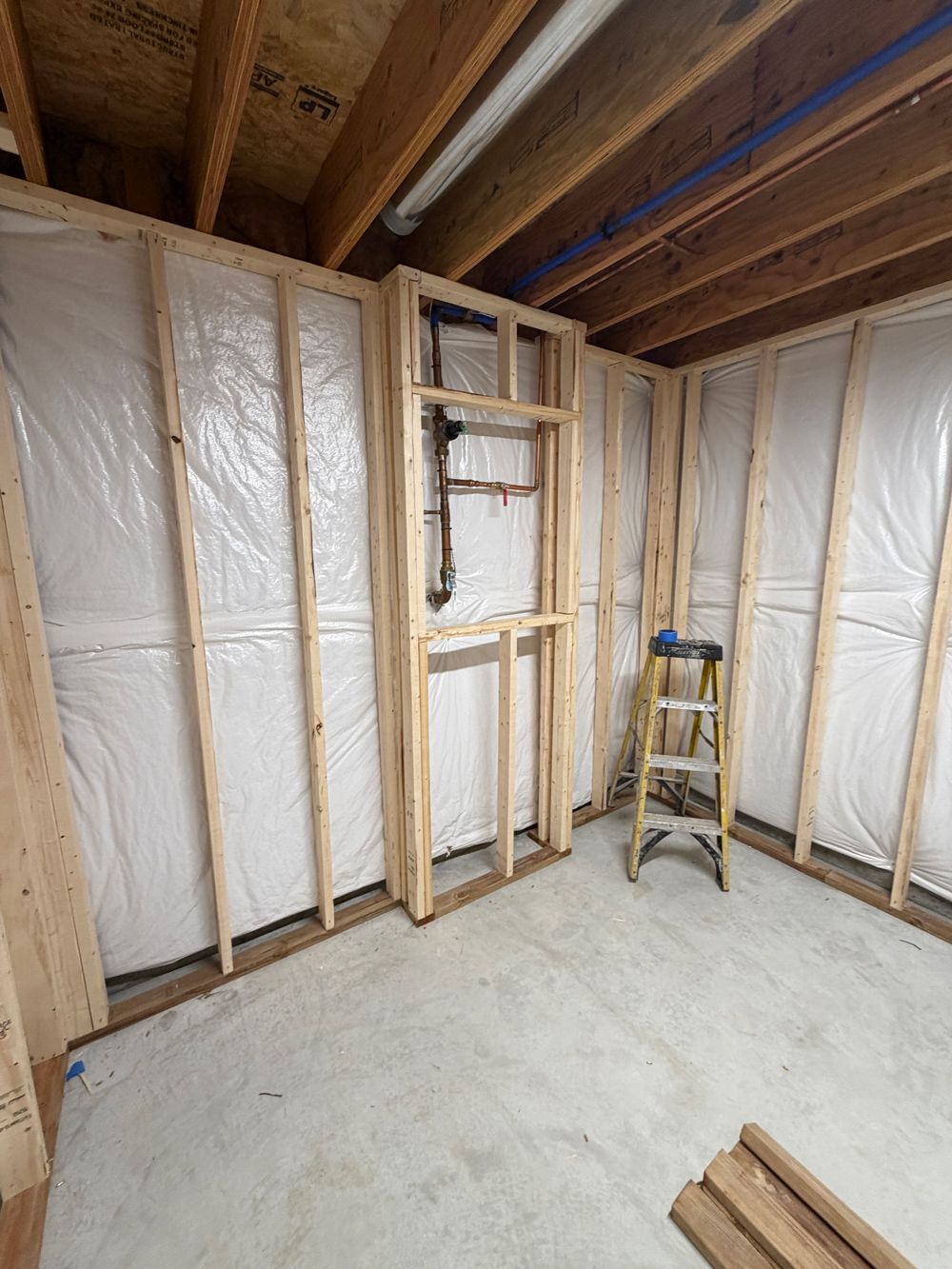 Unfinished basement corner featuring wooden wall framing and plastic vapor barrier over insulation, with a stepladder.