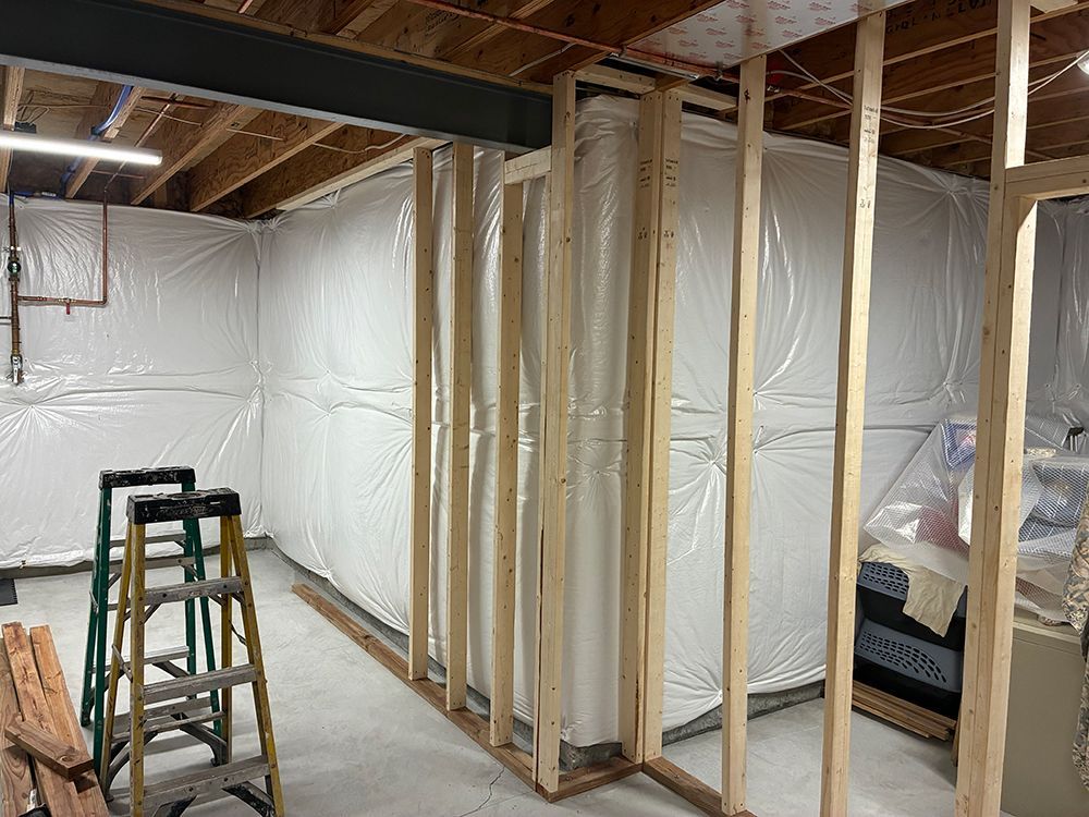 A partially finished basement under construction with wooden wall framing and plastic vapor barriers over the walls.