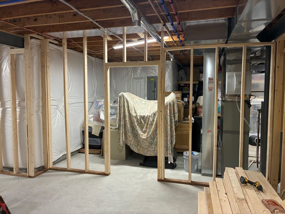 Unfinished basement construction with wood-framed walls and a doorway opening in front of a draped electrical panel.