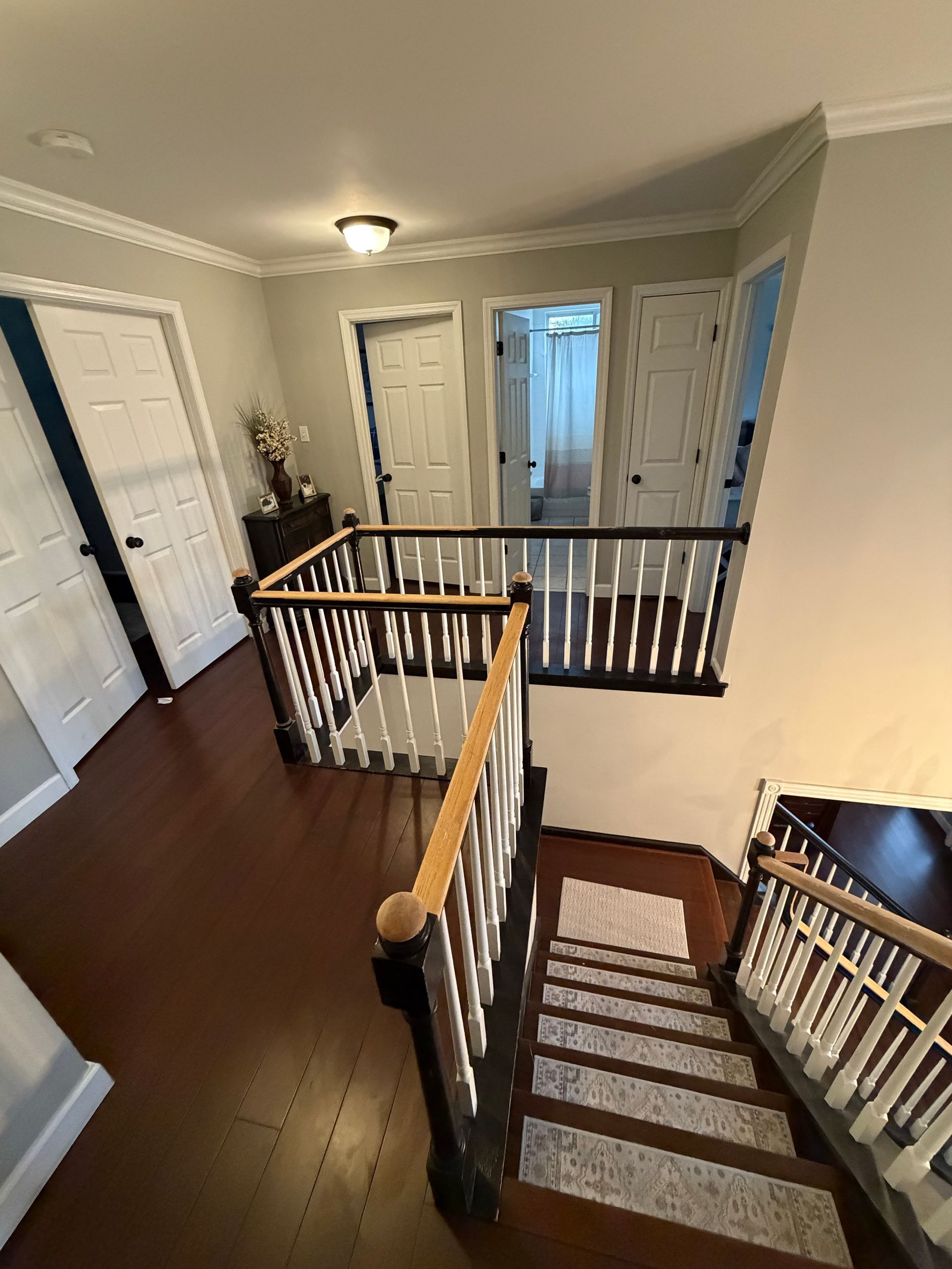 An interior view of an upstairs landing with dark wood floors, white doors, and a staircase with white balusters.