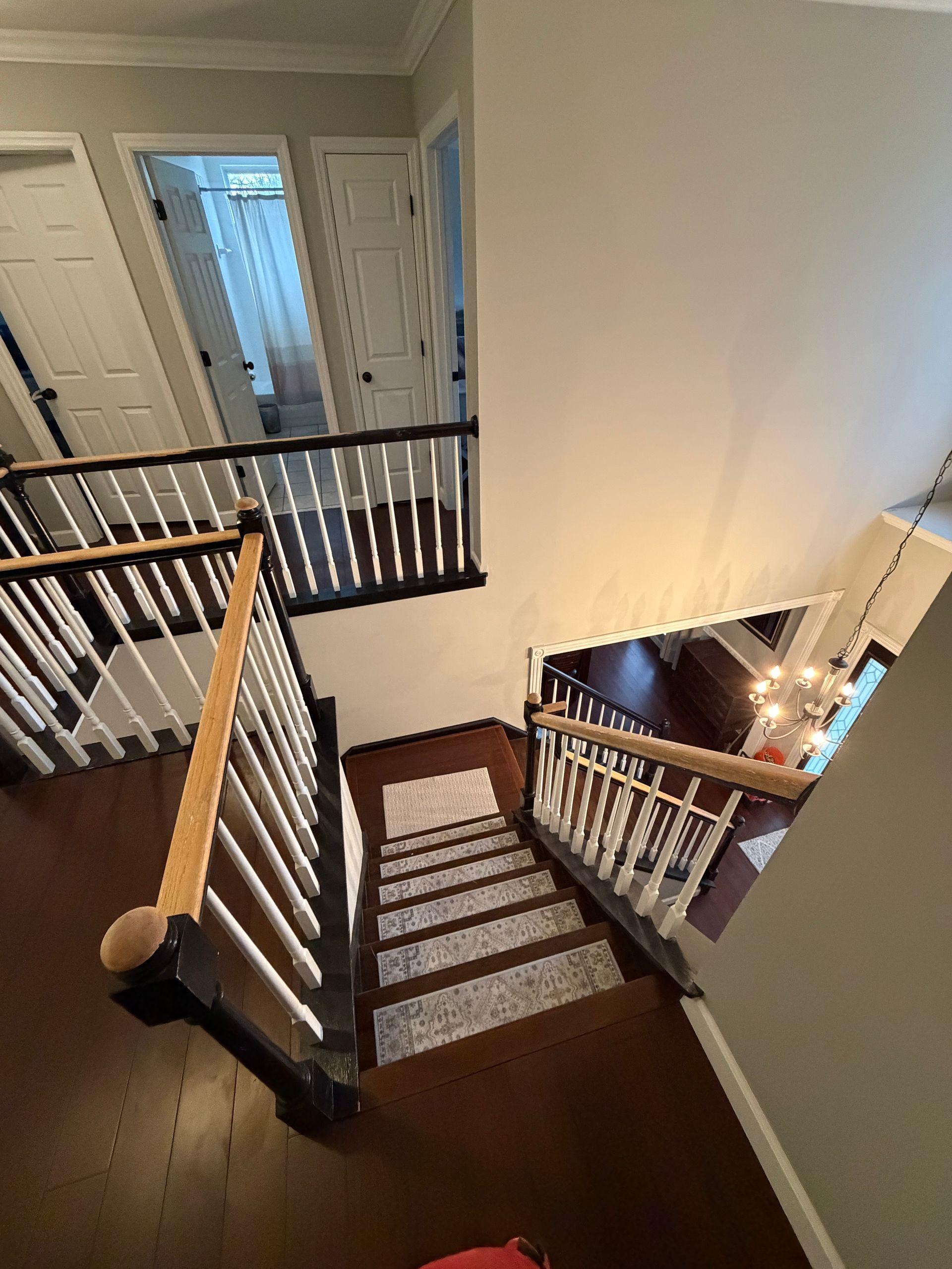 High-angle view of a wooden staircase with a patterned carpet runner, white railings, and an upstairs hallway.