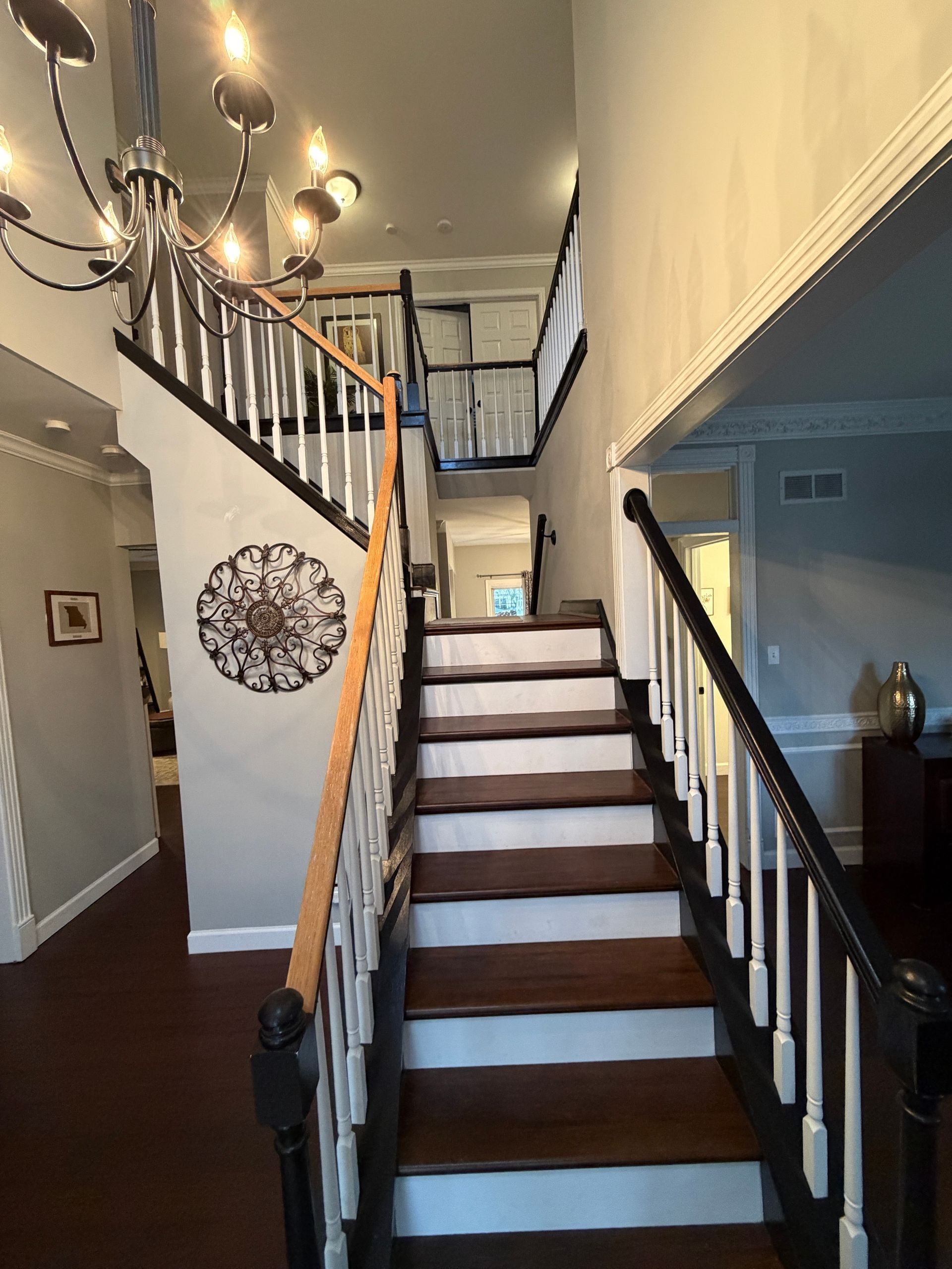 A wooden staircase with white risers and black railings leads to an upper landing under a decorative hanging chandelier.