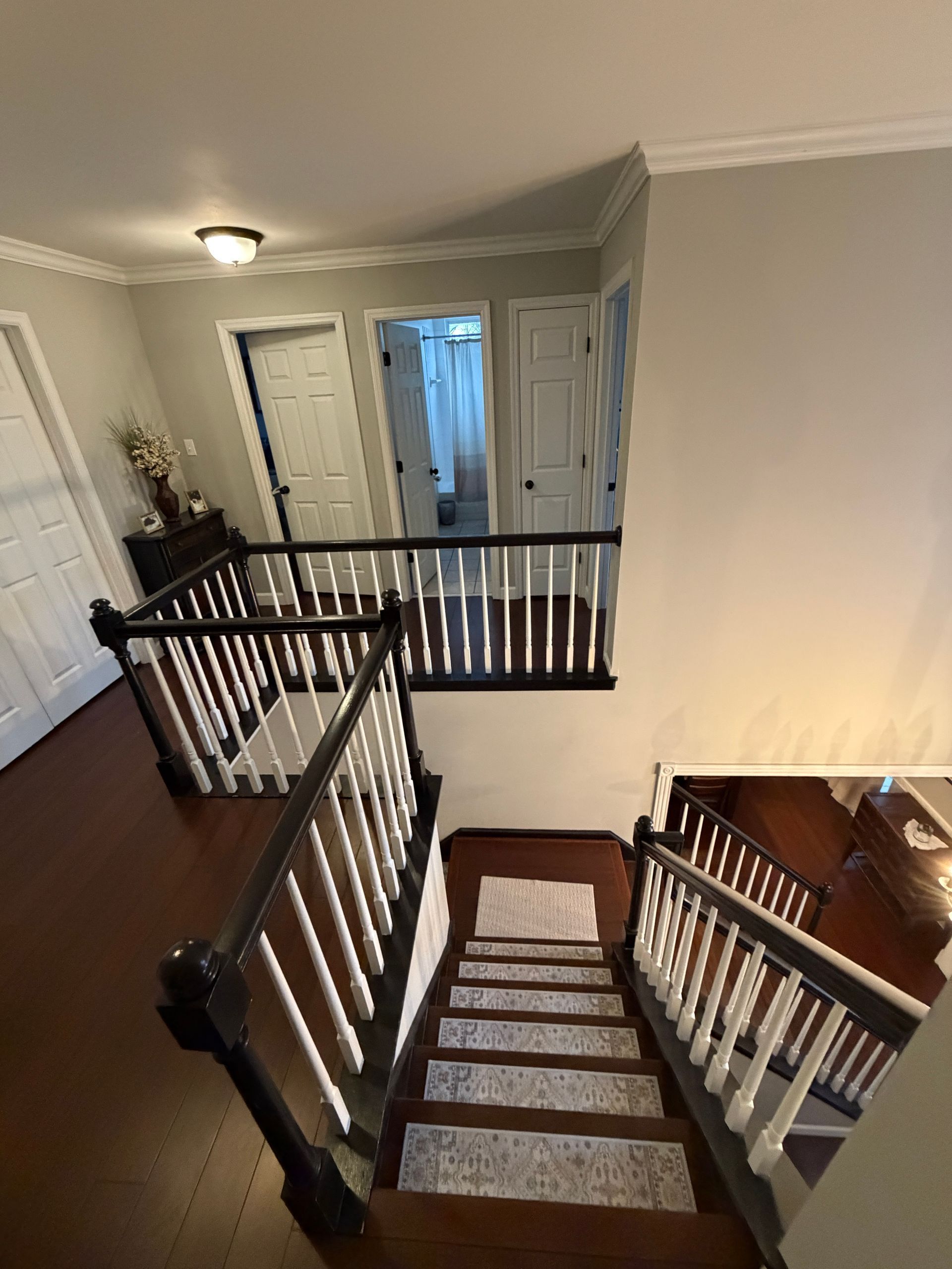 A view looking down a carpeted wooden staircase toward a landing with white doors and black and white railings.