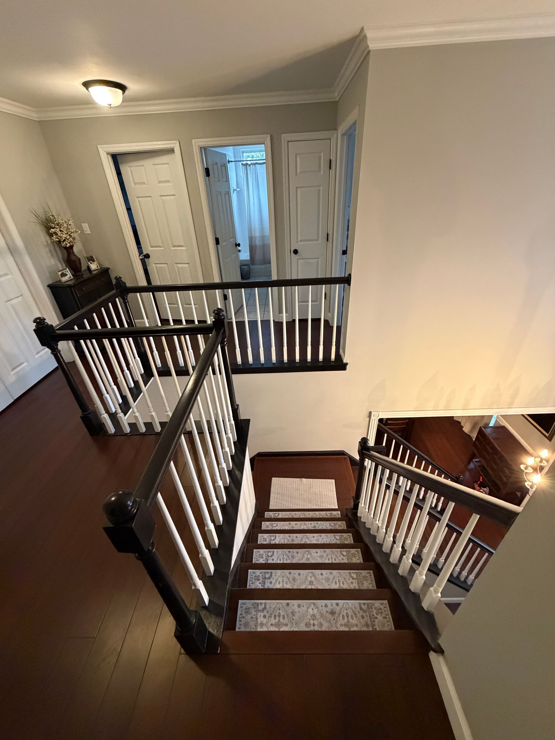 A high-angle view looking down a carpeted staircase with white spindles and dark wooden handrails in a residential hallway.