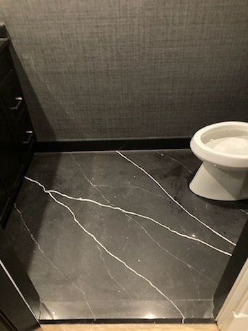 A toilet is sitting on a black marble floor in a bathroom.