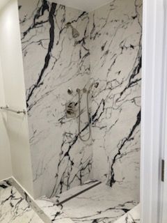 A bathroom with a walk in shower with a black and white marble wall.