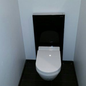 White toilet in a small bathroom with black wall and floor.