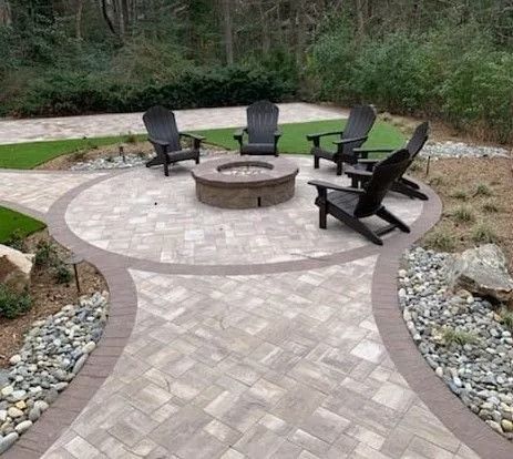 Outdoor patio with fire pit and Adirondack chairs surrounded by pavers and landscaping.