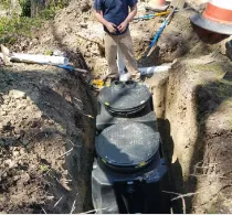Person standing near an excavated septic tank with access lids.