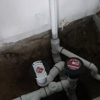 Plumbing pipes with valves and a central vertical pipe in a concrete area.