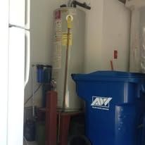 A water heater, blue trash can, and other items in a garage.