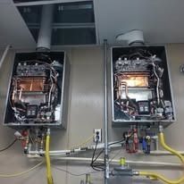 Two tankless water heaters mounted on a wall, with visible internal components.