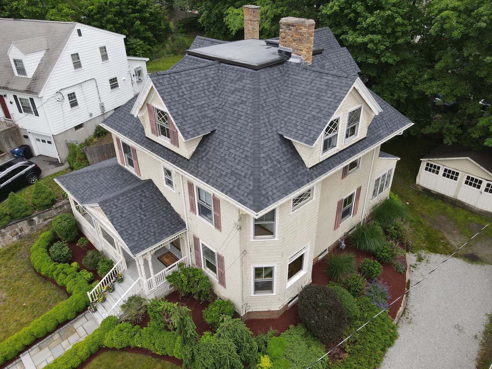 An aerial view of a large house with a gray roof surrounded by trees.