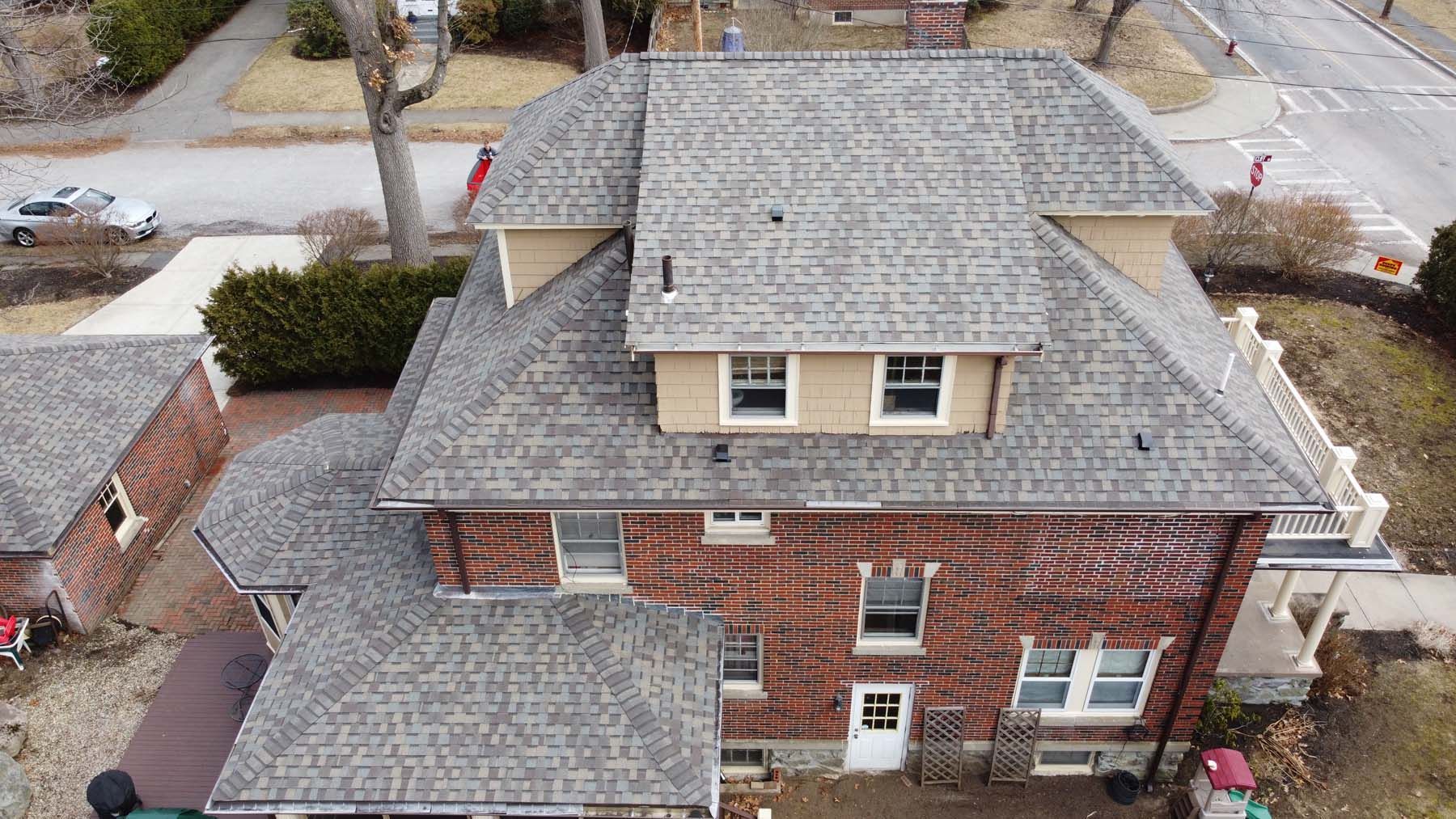 An aerial view of a large brick house with a gray roof.