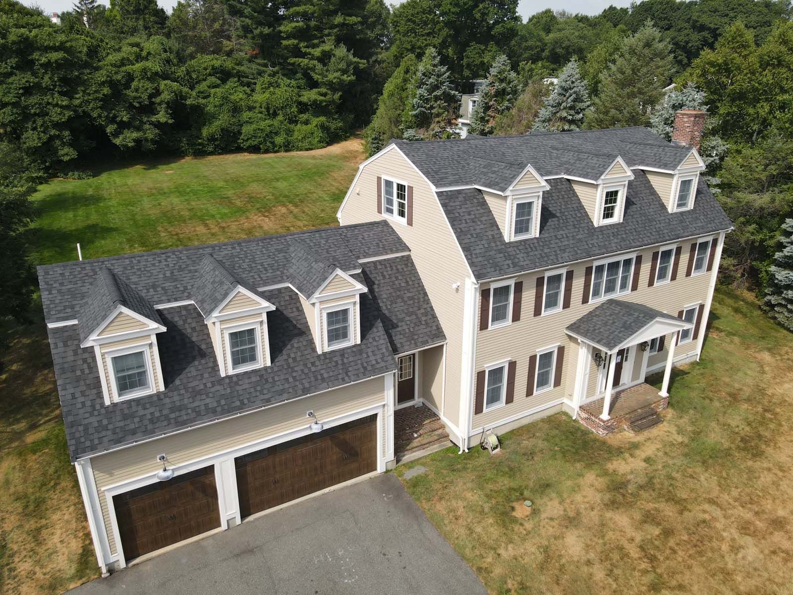 An aerial view of a large white house with a black roof surrounded by trees.