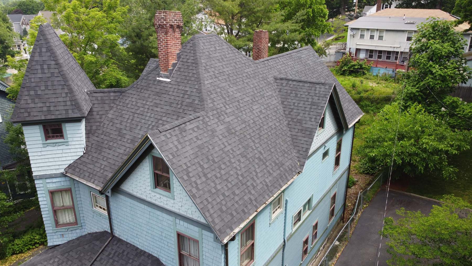 An aerial view of a large blue house with a black roof surrounded by trees.