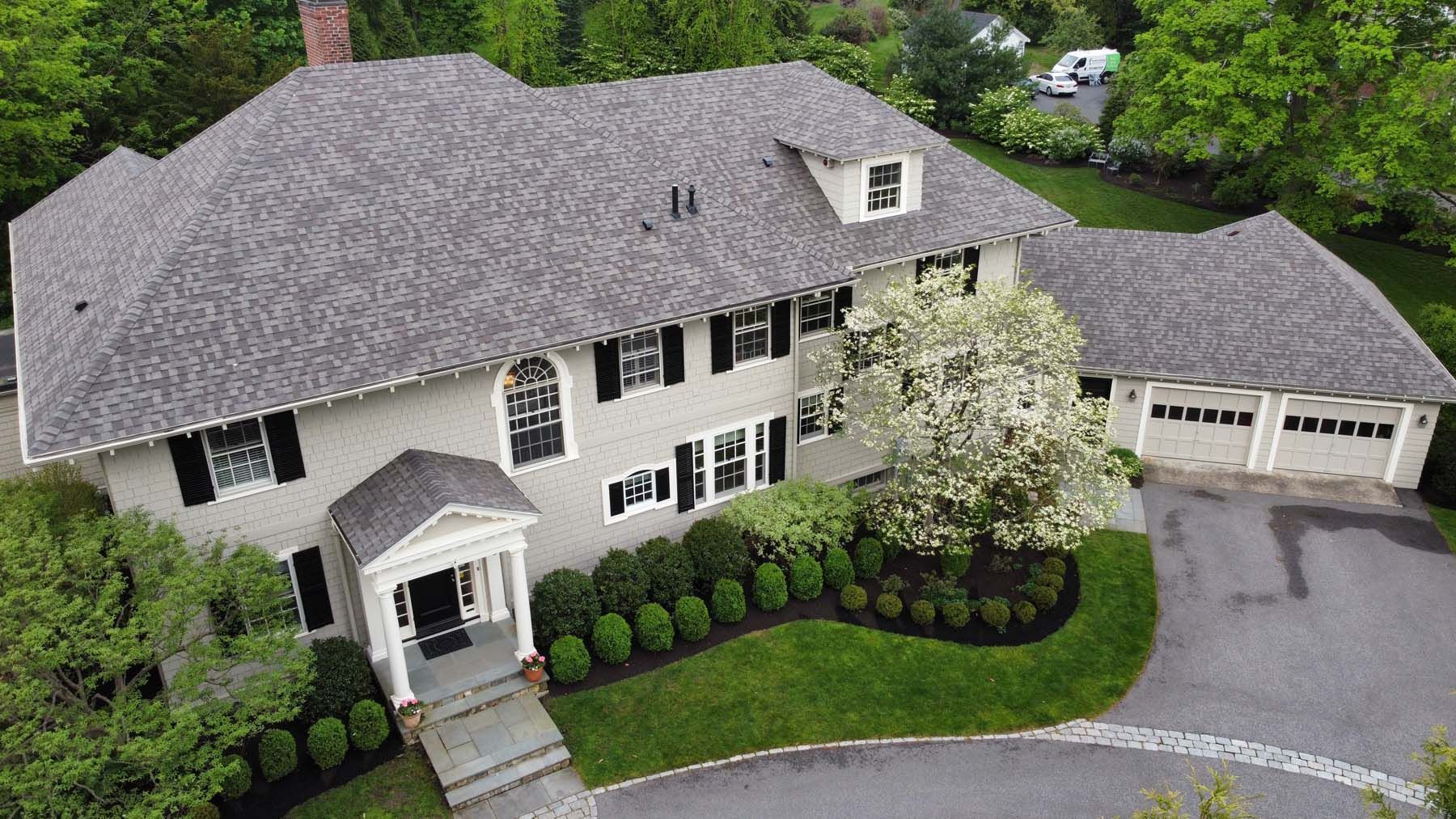 An aerial view of a large white house with a gray roof surrounded by trees.