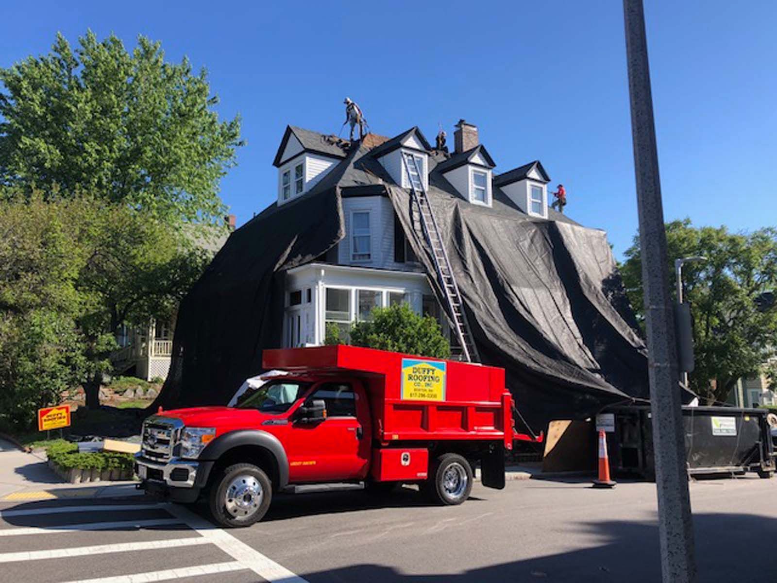 A red truck is parked in front of a house with a tarp on the roof.