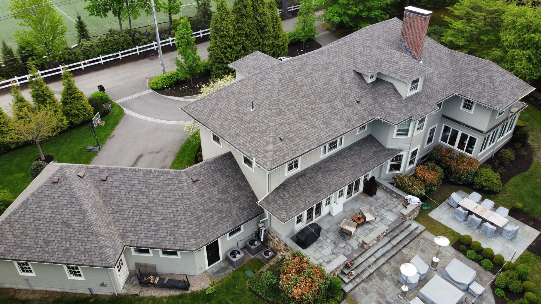 An aerial view of a large white house with a gray roof surrounded by trees.