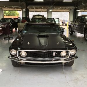 A black mustang is parked in a garage with other cars