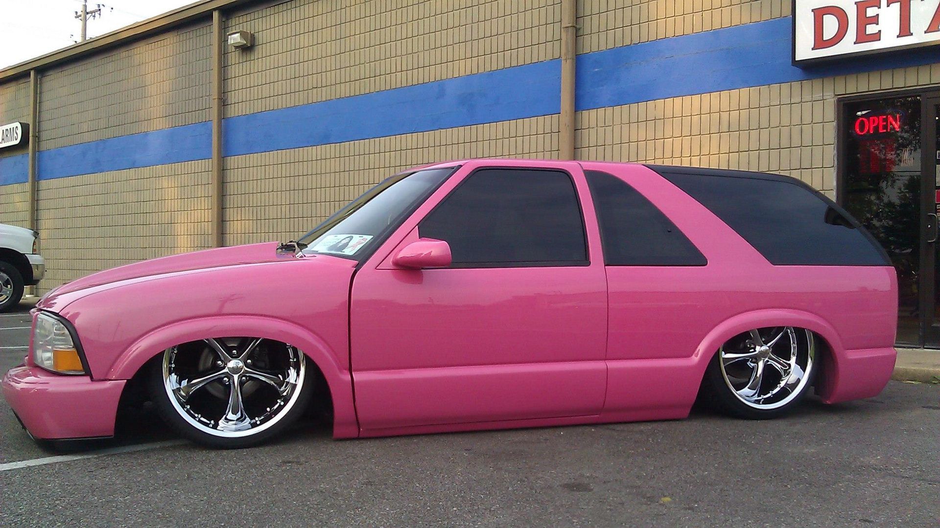 A pink car is parked in front of a storefront.