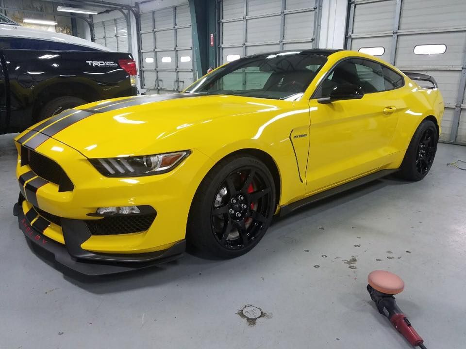 A yellow ford mustang is parked in a garage next to a polisher.