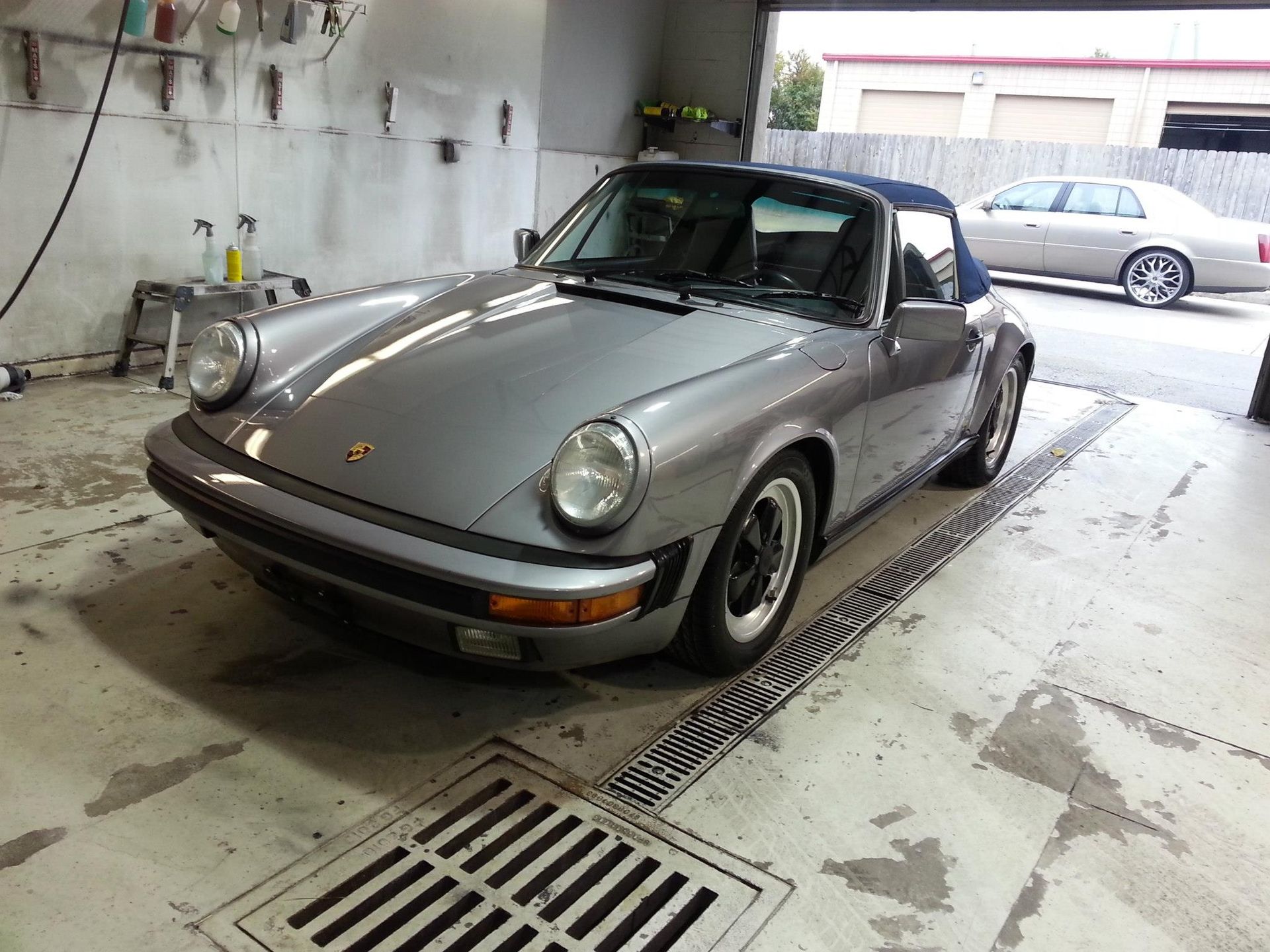 A silver porsche 911 convertible is parked in a garage.