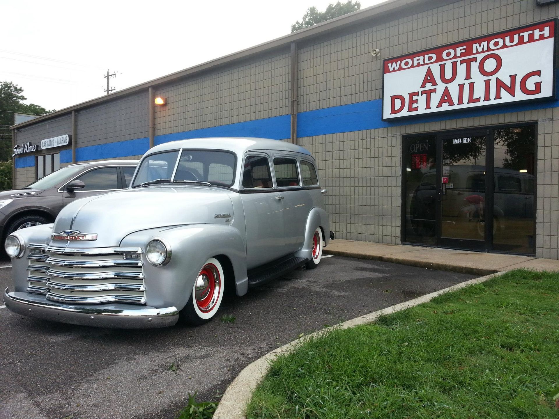 A silver car is parked in front of a building that says auto detailing.