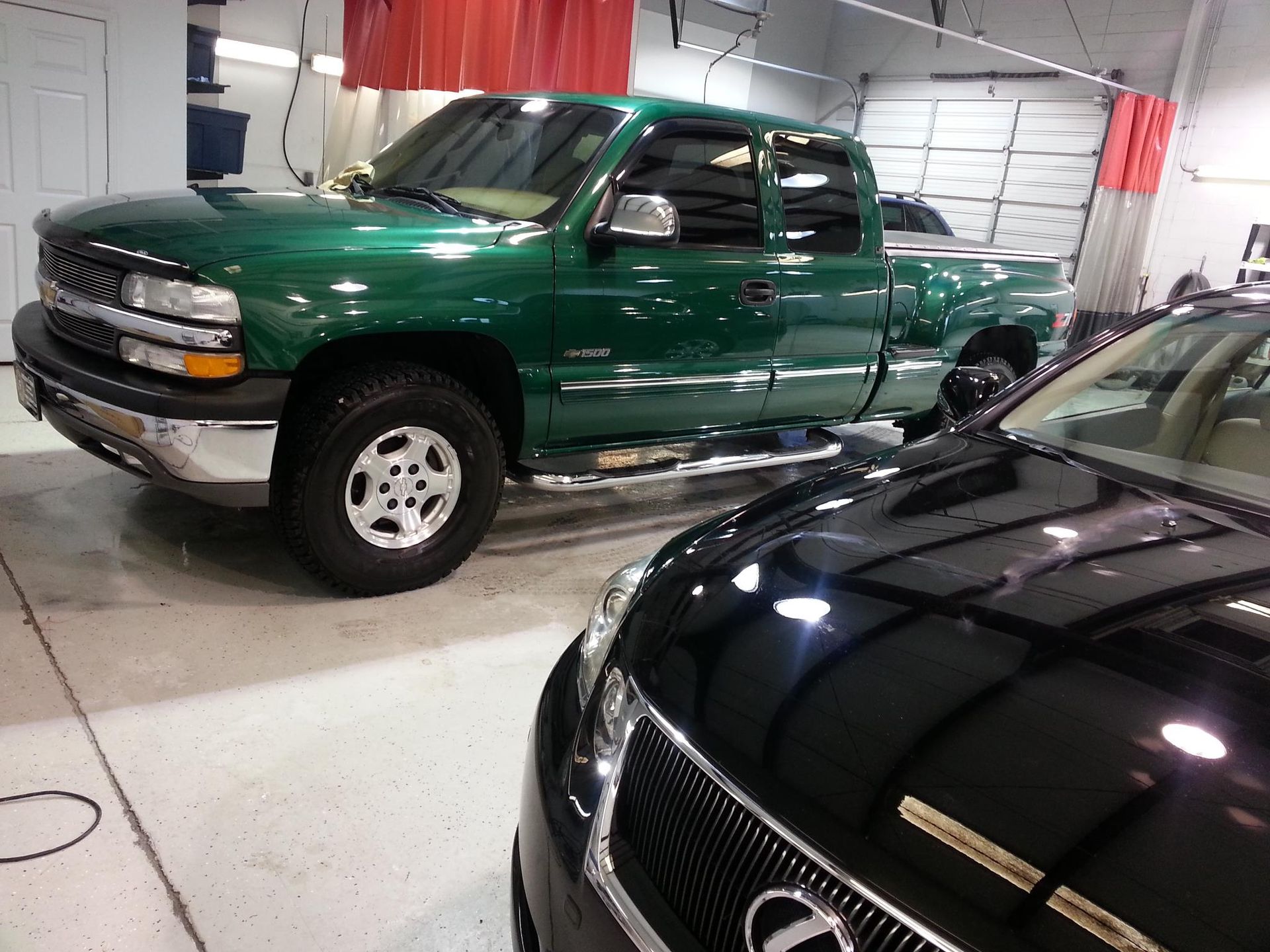 A green truck is parked next to a black car.