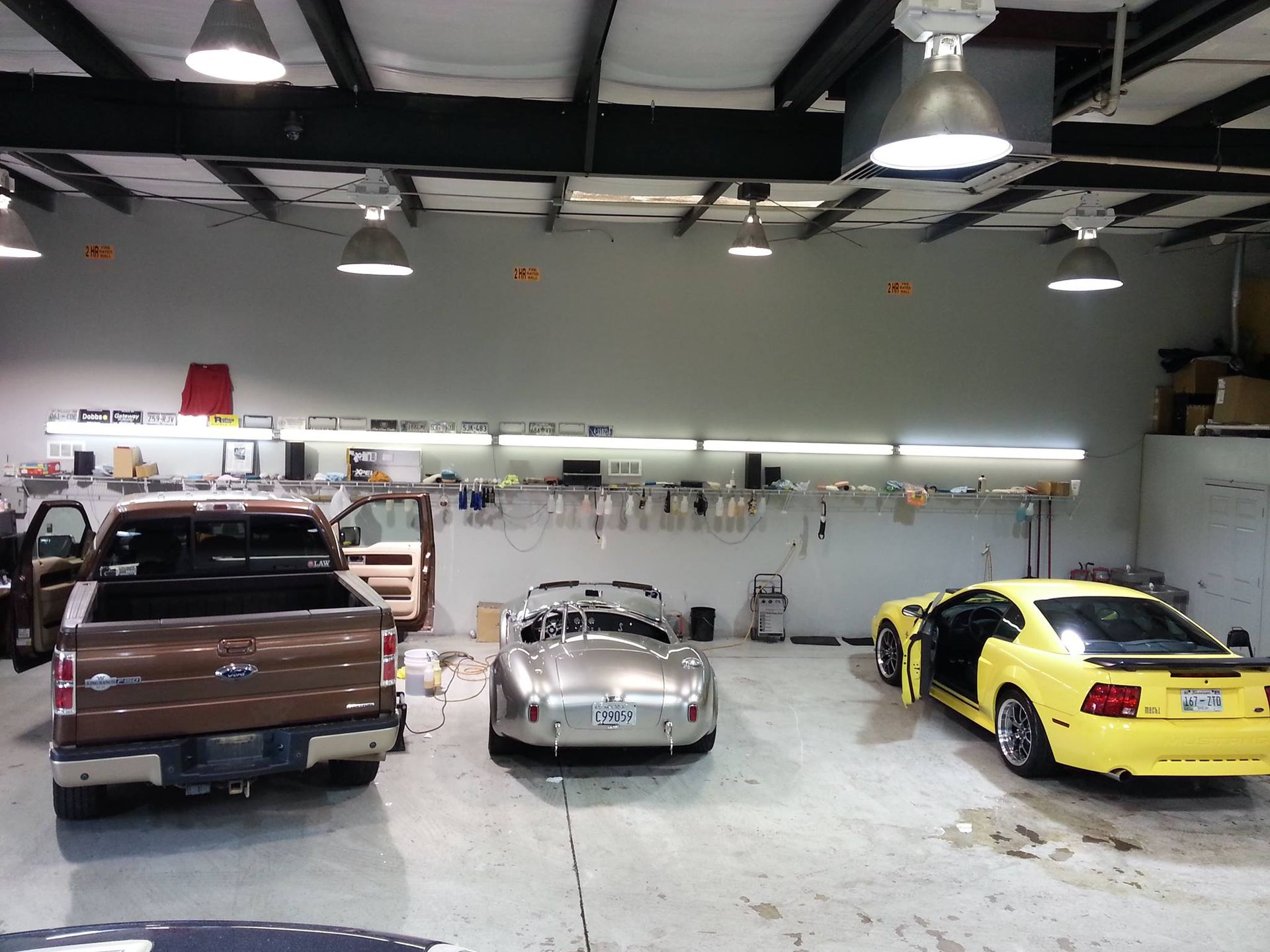 A ford truck is parked in a garage next to two sports cars.