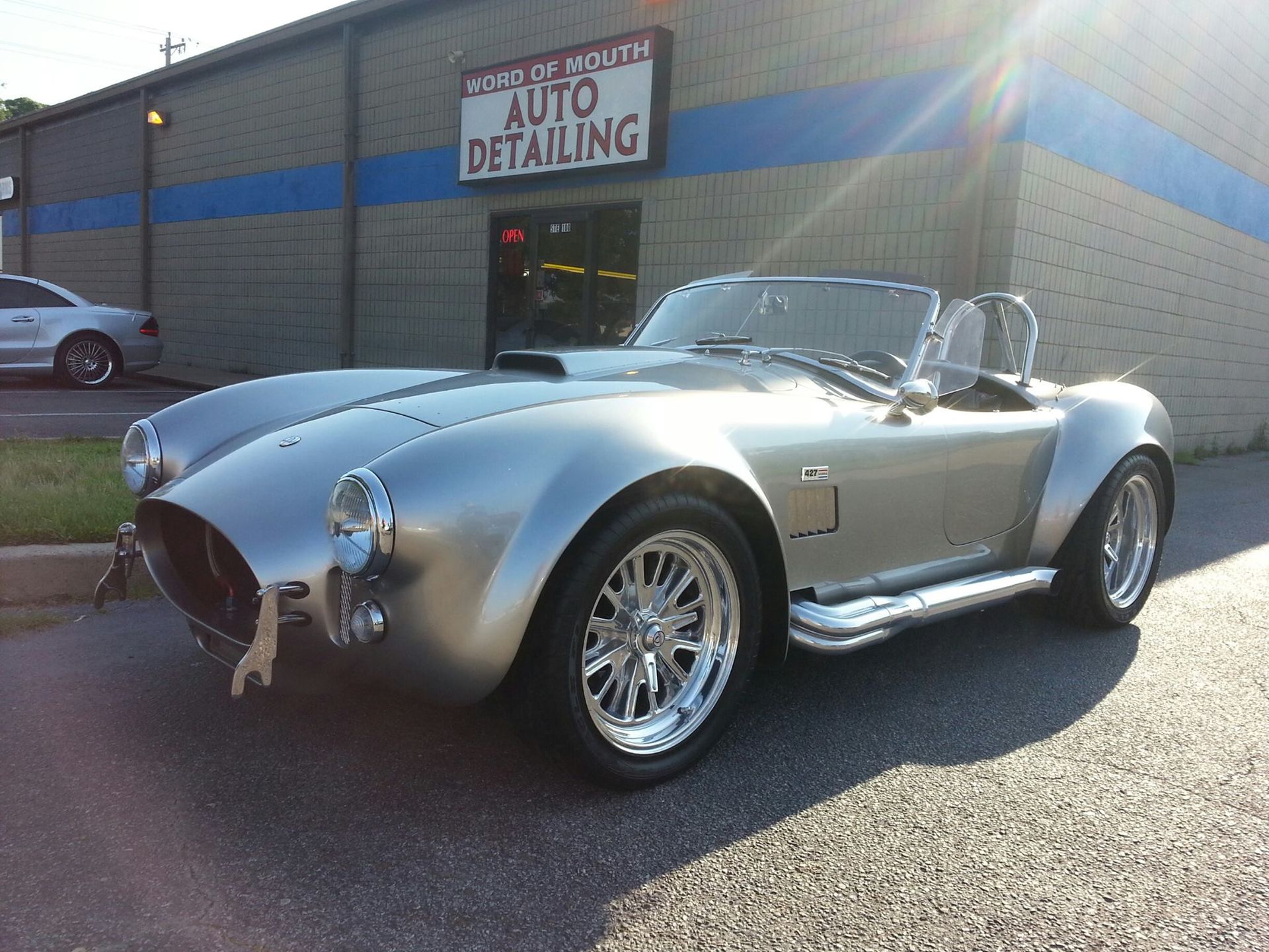 A silver car is parked in front of a building that says auto detailing.
